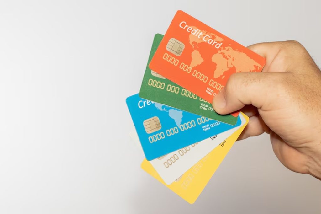 Close-up of a hand holding a fan of colorful credit cards against a neutral background — a visual representation of the comparison between cards with fixed cashback and cashback by category.