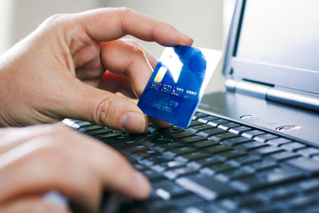 Close-up of a person holding a blue credit card above a laptop keyboard, ready to complete an online transaction — illustrating the growing role of digital signatures in secure e-commerce authentication.