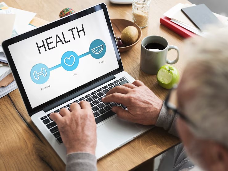 An older man using a laptop at a wooden table, viewing a screen with icons representing exercise, life, and food—highlighting the importance of personal care and health in everyday routines.
