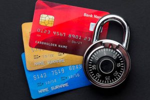 Three colorful credit cards stacked beneath a metal combination lock on a dark surface — a symbolic representation of financial safety and the role of secured cards in building credit responsibly.